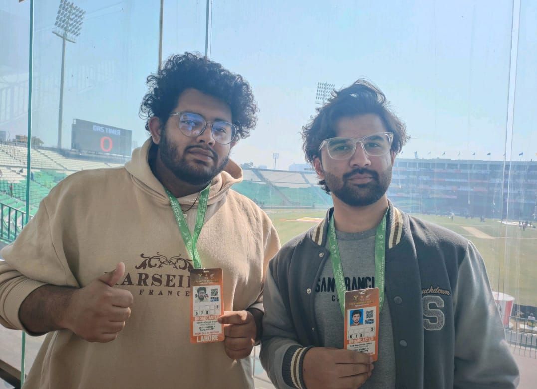 Two Chrio team members with broadcaster accreditation in a stadium broadcast box, DRS timer visible